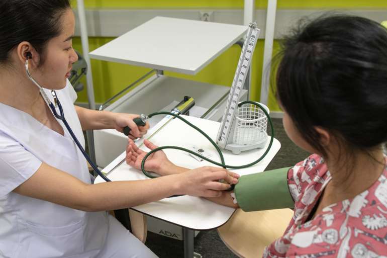 Opiskelija mittaa toiselta henkilöltä verenpainettta.